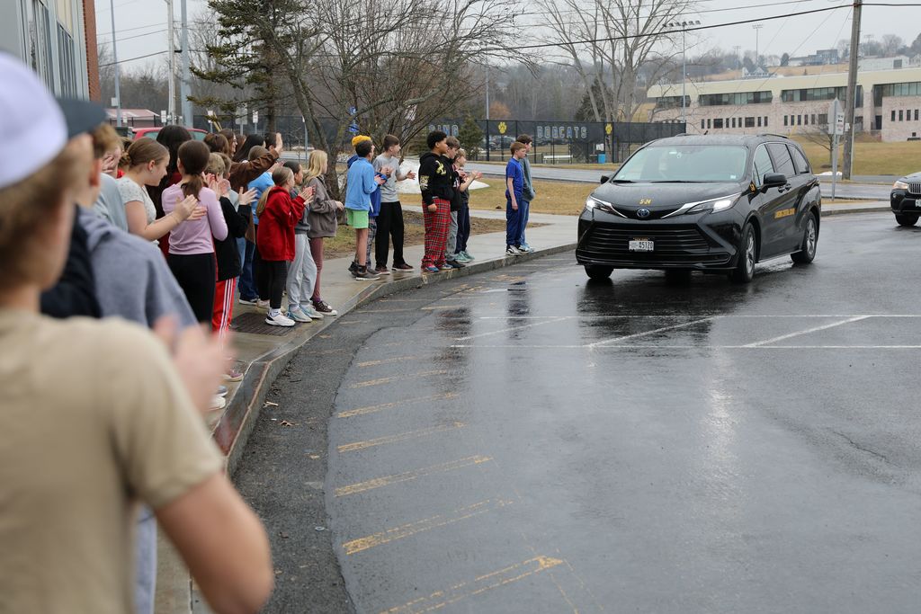 a an driving by a bunch of young students as they cheer it on