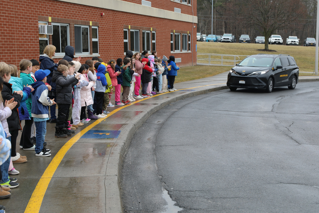 the van drives by a large group of young students as they cheer it on