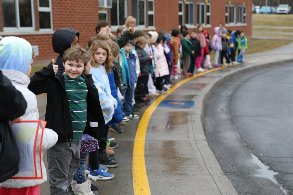 a student gives the thumbs up as him and many others wait for the van to drive by