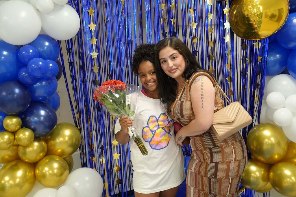 A fourth grade student holds a bouquet of red roses while posing with a family member after the Moving Up Ceremony.