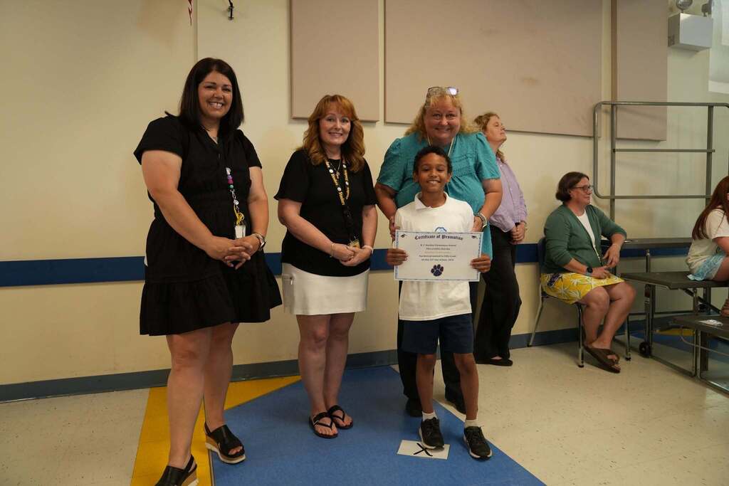 A fourth grade student holds a promotion certificate while posing with three school staff members during the Moving Up Ceremony.