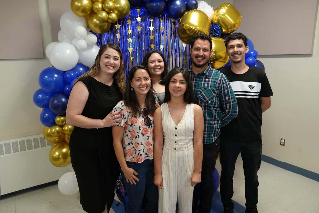 A fourth grade student poses with family members in front of a blue and gold balloon display following the Moving Up Ceremony.
