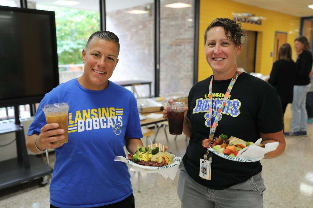 two staff members holding up their plates of food
