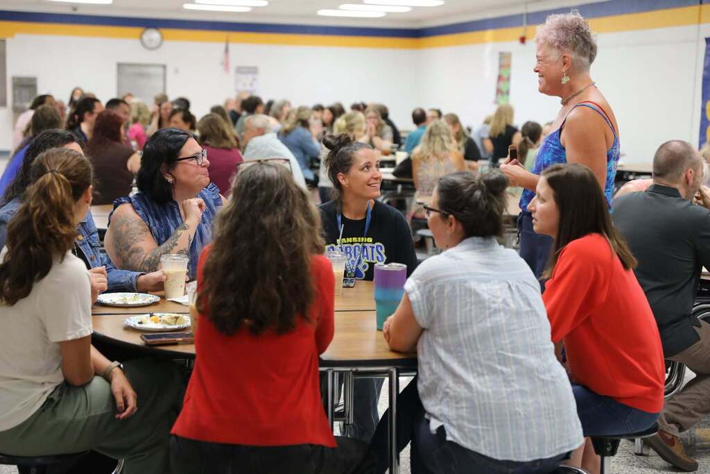 crowd of people at a table talking without someone standing