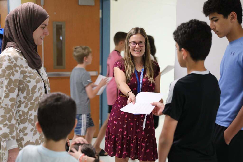 a teacher handing a student some papers while smiling