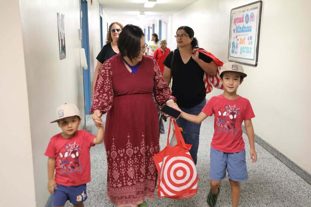 a parent leading their two kids down a hall