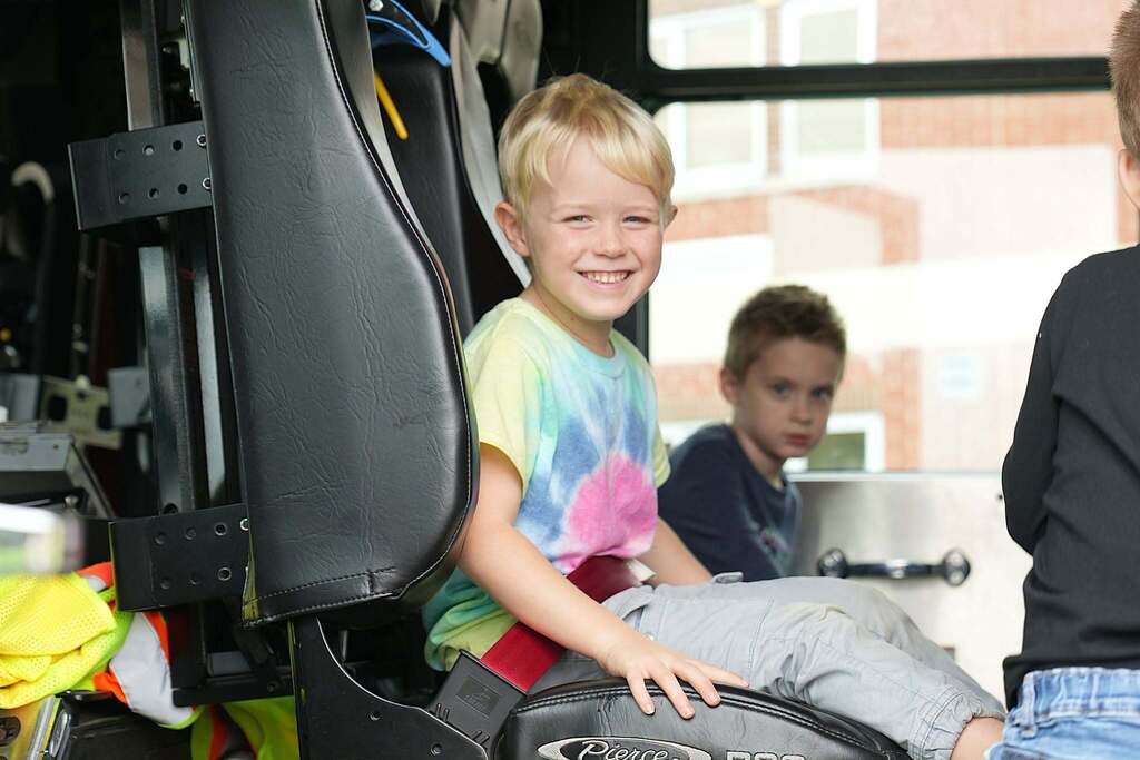 A young boy in a tie-dye shirt smiles happily while sitting inside a Lansing Fire Department truck.