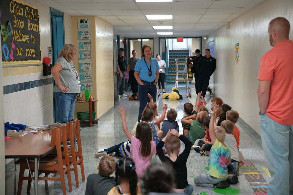 Kindergarten students sitting in a school hallway with their hands raised during a fire safety presentation