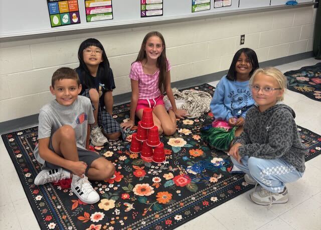 Students playing cup stacking on a rug in a classroom