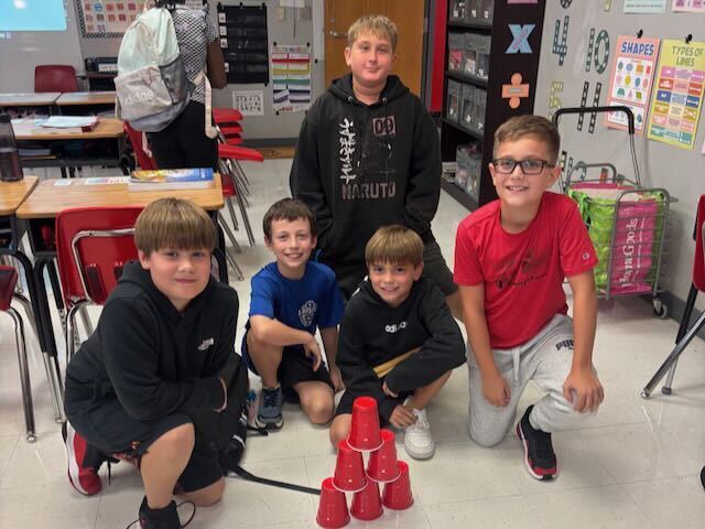 Students playing cup stacking on a rug in a classroom