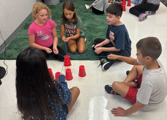 Students playing cup stacking on a rug in a classroom