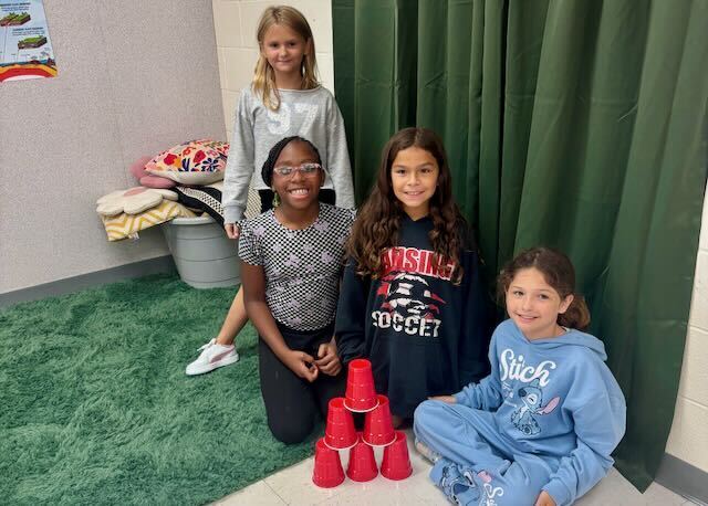 Students playing cup stacking on a rug in a classroom