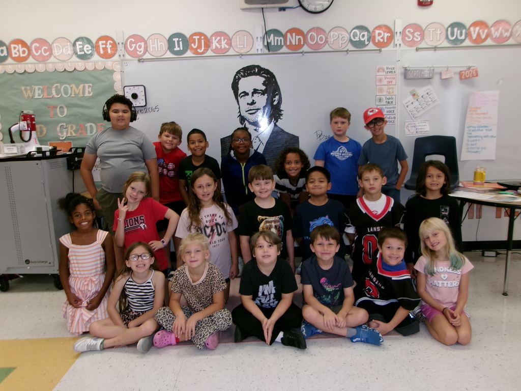 third grade class smiling in front of white board with drawing of Brad Pitt