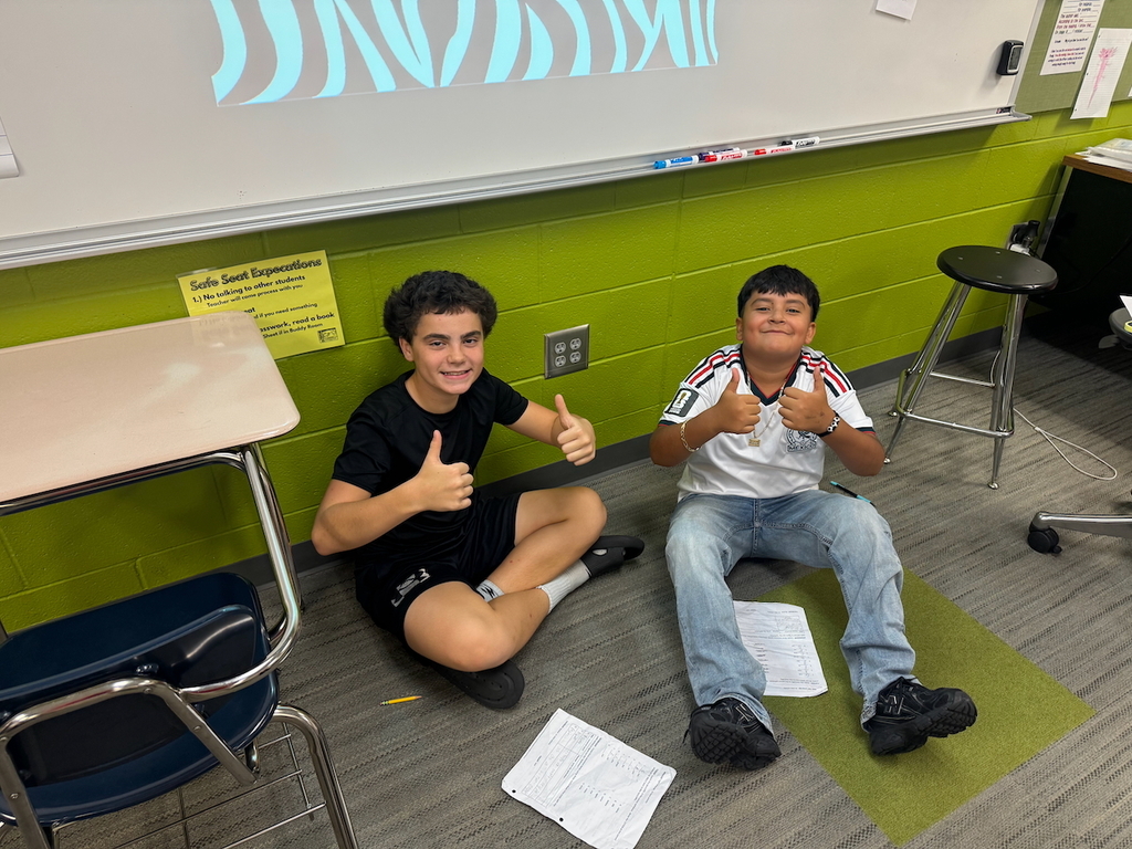Two students smiling in a classroom giving a thumbs up