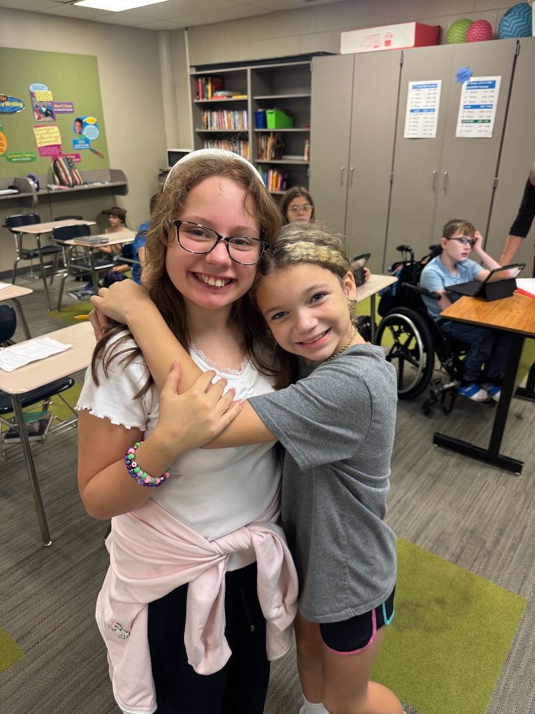 Two students smiling and hugging in a classroom