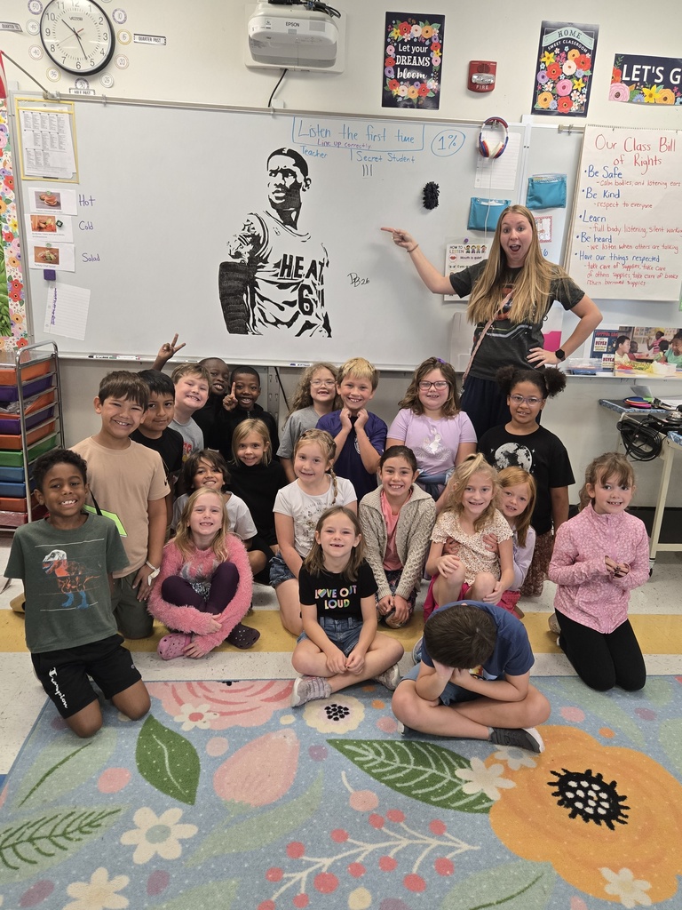 2nd grade students and teacher posing in front of white board with artwork
