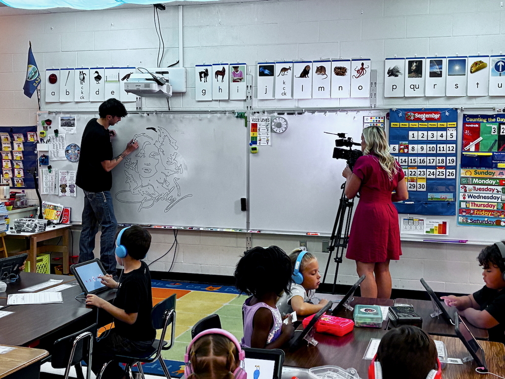 Custodian being interviewed on camera while creating artwork on whiteboard