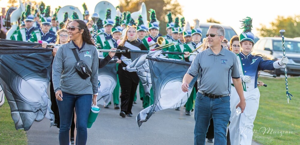 Lapeer band directors Alexis Johnson and Dan Hundt leading the marching band onto the field