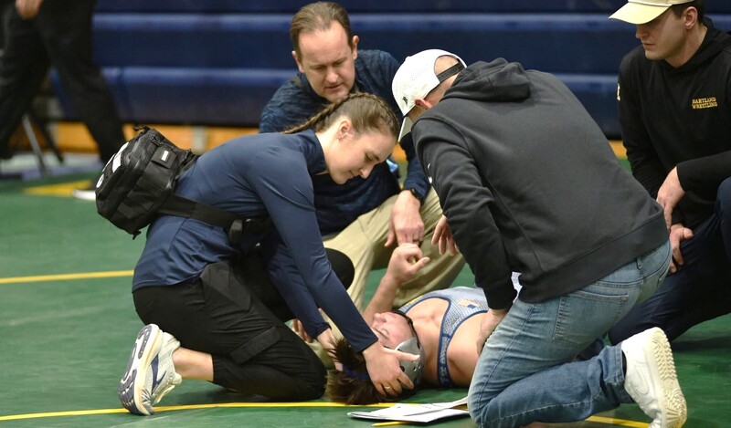 Female athletic trainer tending to injured high school wrestler