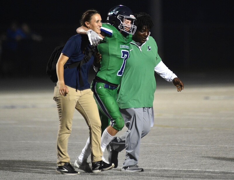 Female athletic trainer helping a Lapeer football player off the field.
