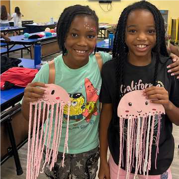2 girls holding pink paper jellyfish with string tentacles 