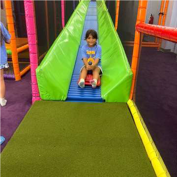 girl riding a small red cart down a long slide