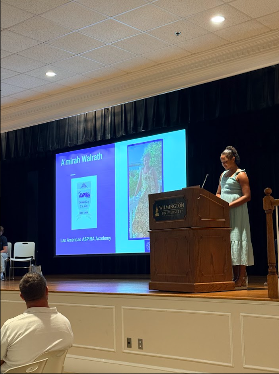 A'mira speaking at podium at AVID event with her picture on monitor 