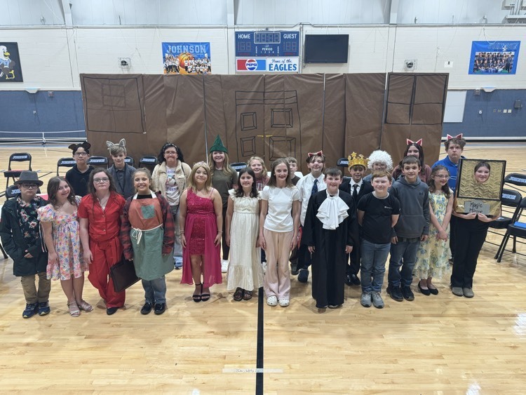 Boys and girls in a variety of costumes stand in front of their set in the Johnson Elementary gym  