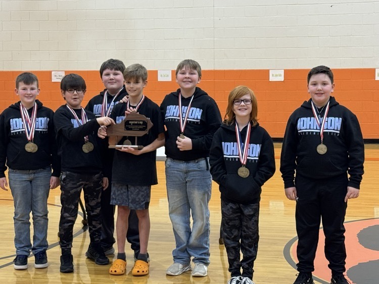 Seven boys in black Johnson Elementary academic team shirts stand together in a gym with a Kentucky-shaped trophy  