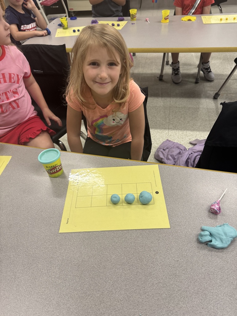 Student smiling with three balls of teal play-dough on a number grid