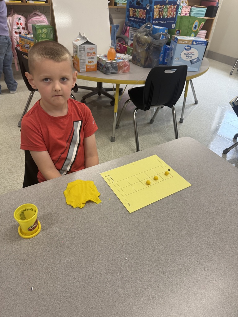 Student looking at camera with three balls of play-dough on number gird and a large blob of yellow play-dough on table