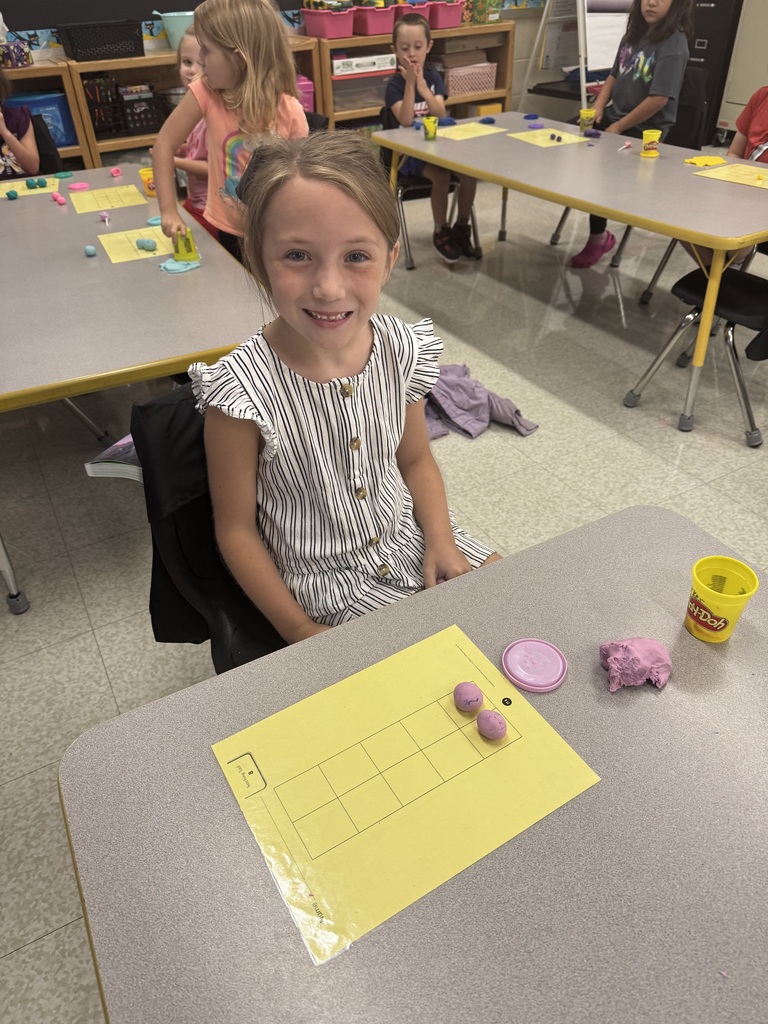 Student smiling with two balls of light purple play-dough on a number grid