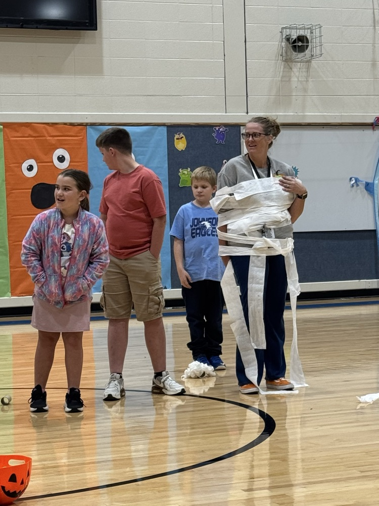 three students wrap a teacher in toilet paper as part of a mummy themed game.