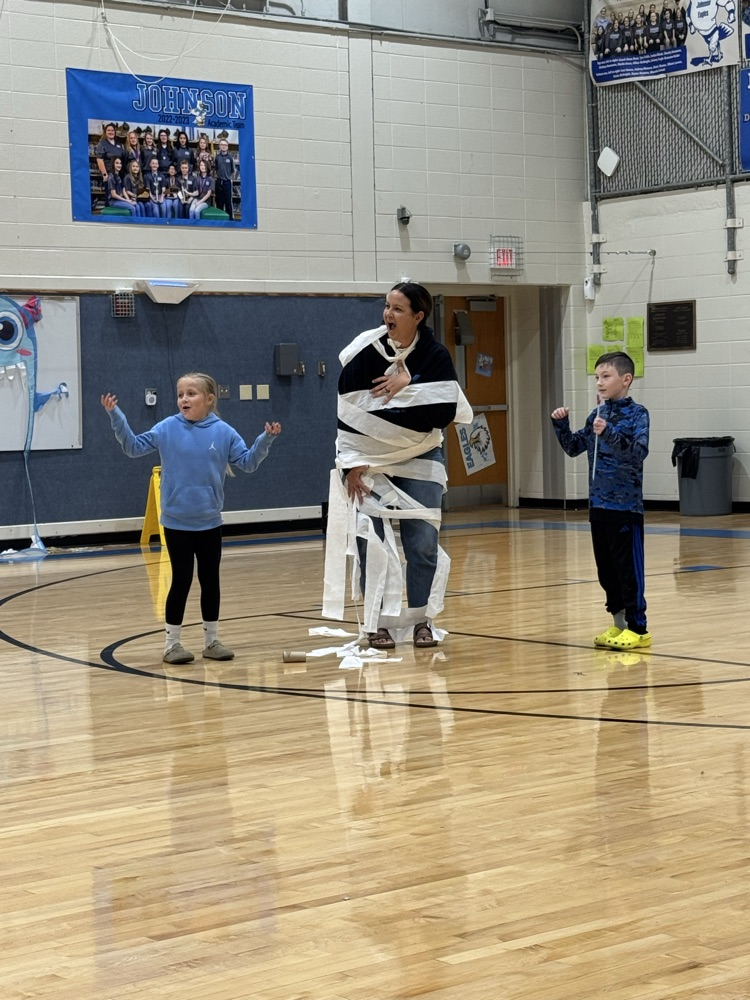 three students wrap a teacher in toilet paper as part of a mummy themed game.
