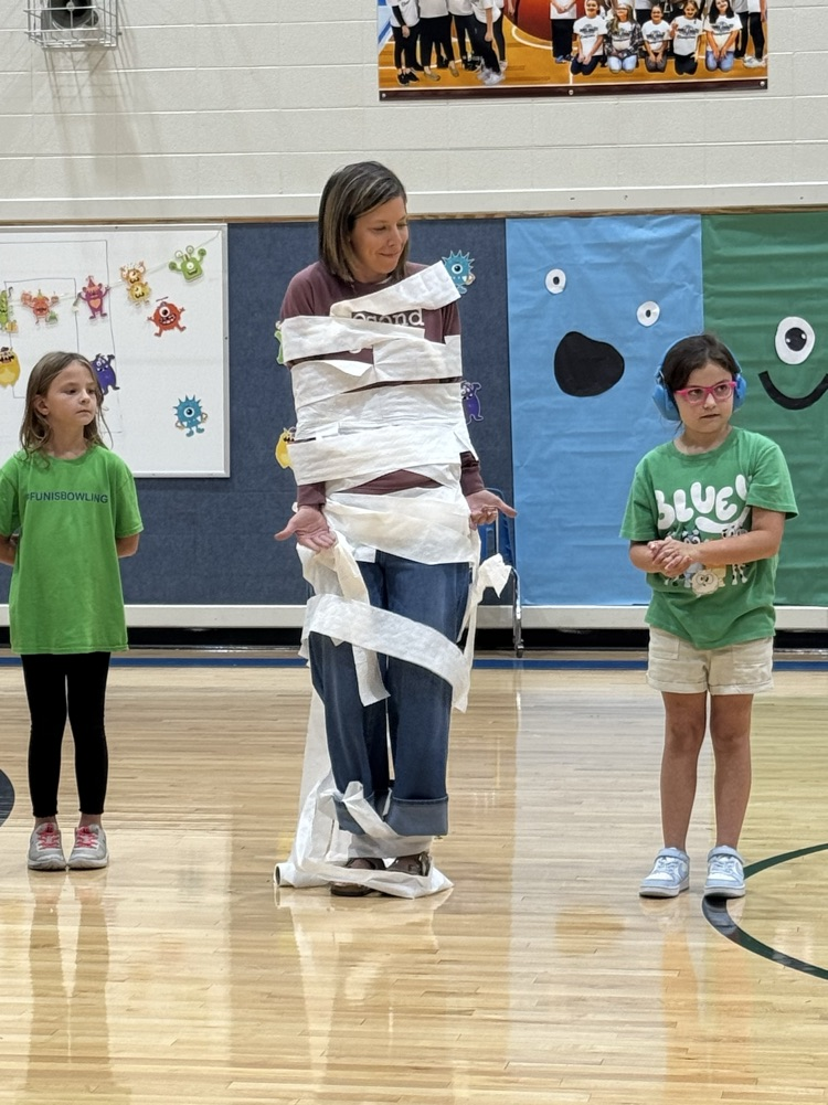two students wrap their teacher in toilet paper as part of a mummy themed game.
