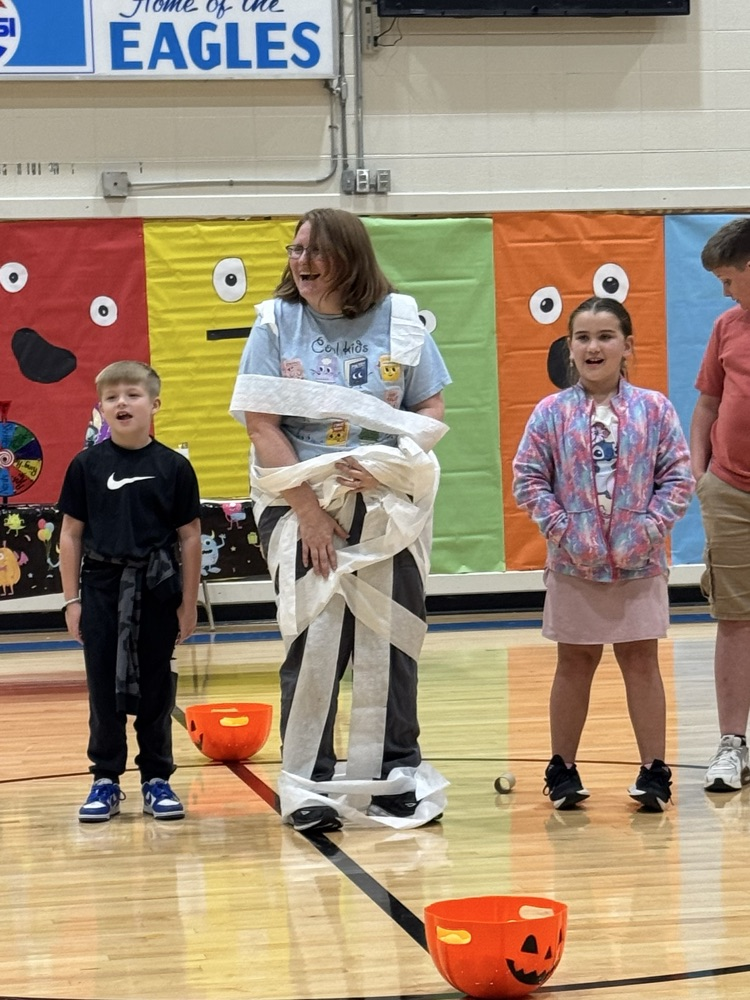 three students wrap a teacher in toilet paper as part of a mummy themed game.