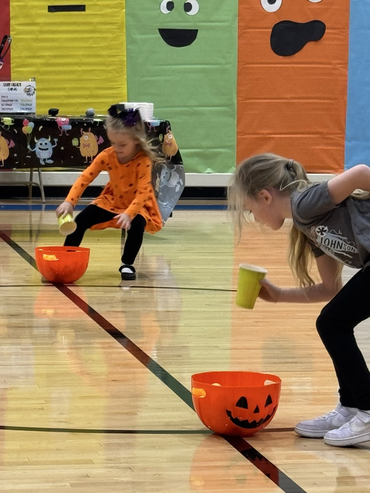 Two girls race to pumpkin decorated bowls to pick up ping-pong balls.