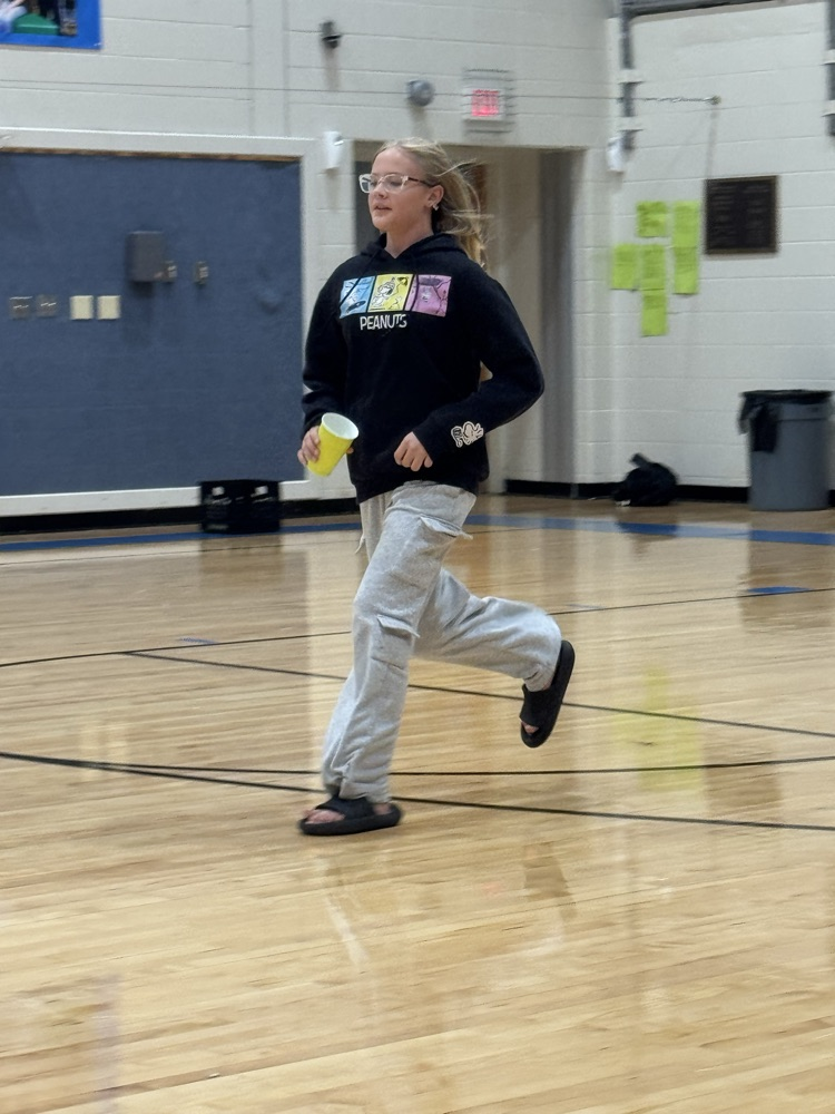A blonde girl in a black hoodie runs across a gym floor.