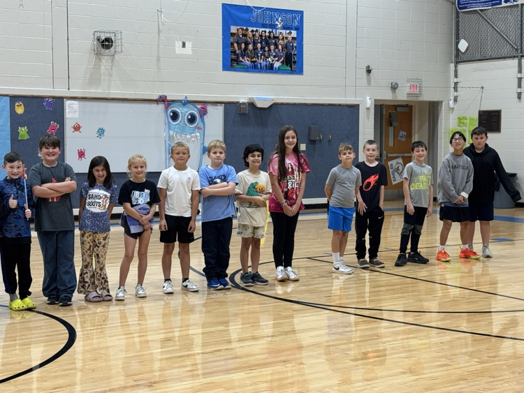 Smiling elementary school students stand in one line in the gym for their picture.