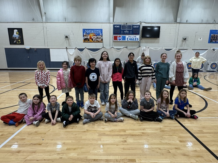 This group of students represents the the person in each class with the most reading i-Ready lessons and the most math I-Ready lessons. They are arranged in two rows with the front row, sitting on the gym floor and the back row standing behind them.