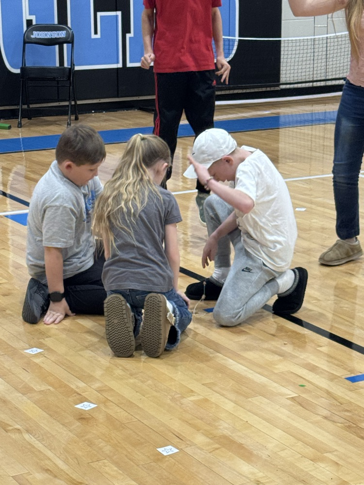 Students sit on the gym floor in a circle and play a game in which they have to put Cheerios on a piece of string.