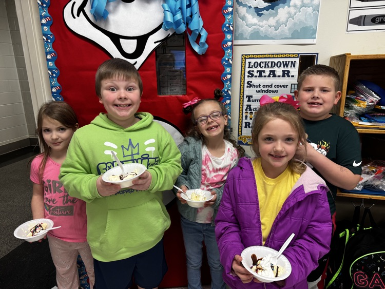 Four elementary students smile for the camera while holding ice cream sundaes  