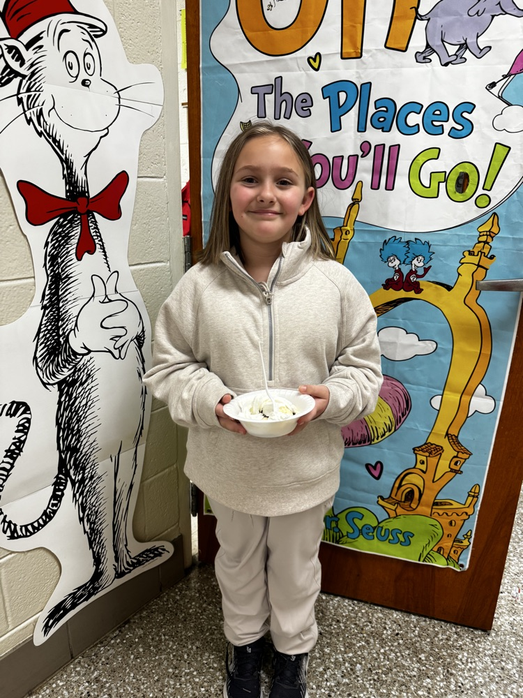 A young girl in a light gray sweatsuit smiles while holding an ice cream sundae  