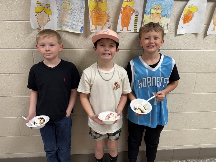 Three boys smile for the camera while holding ice cream sundaes. 