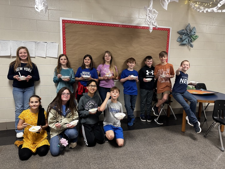A group of several young students smiles for the camera while holding ice cream sundaes. 