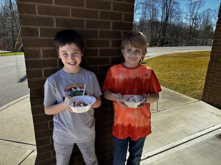 Two boys smile for the camera while holding ice cream sundaes. 