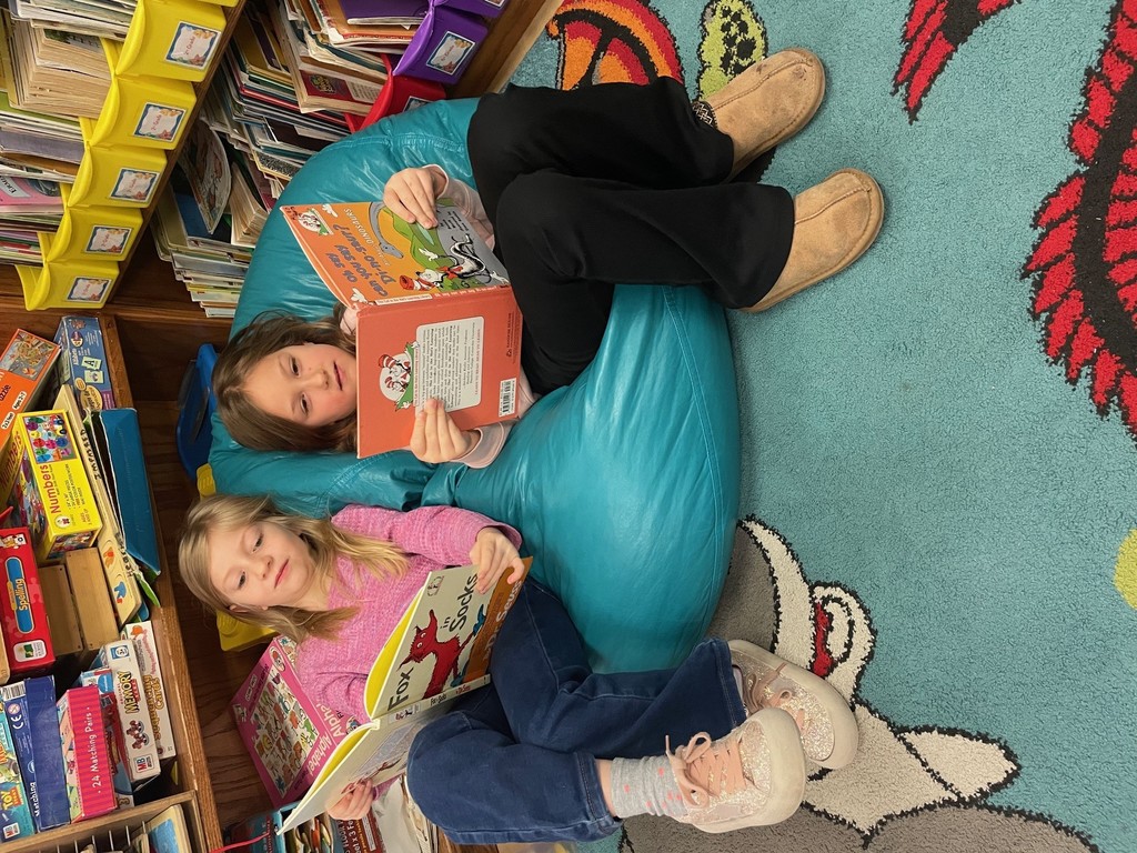 Two students reading books while sitting on bean bags in the library
