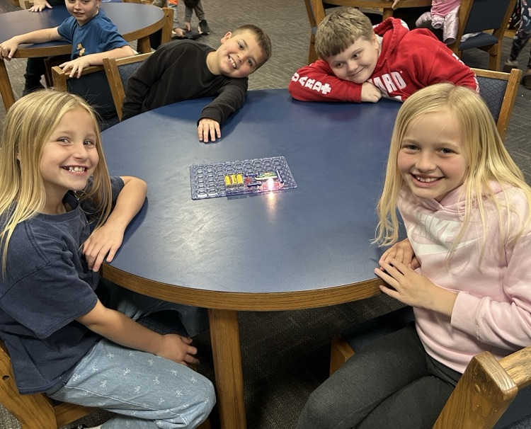 Four students smile for the camera as they sit around a round, blue table using a snap circuit set