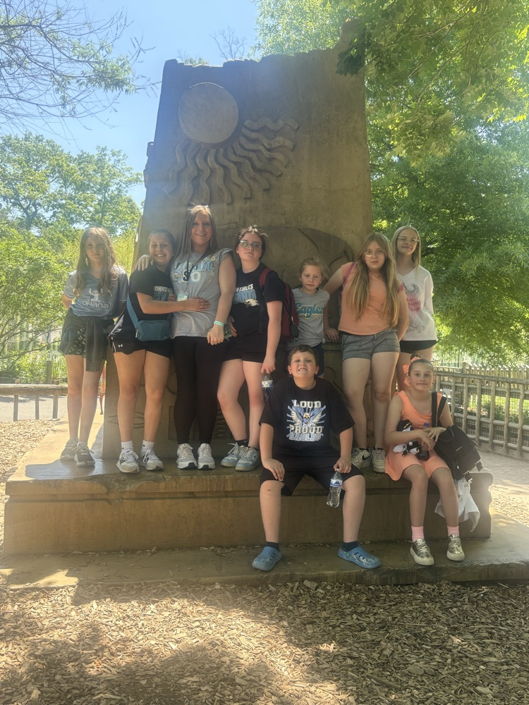 A group of students pose for a picture info front of a zoo statue  