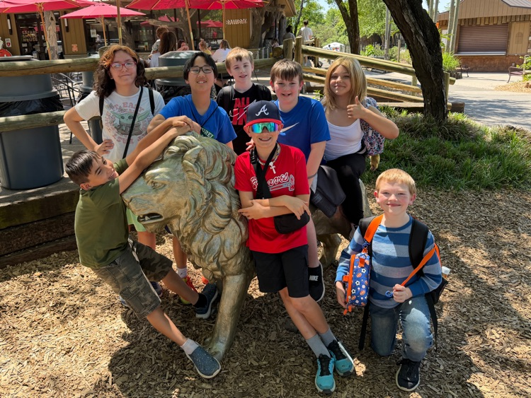 A group of students pose for a picture with a bronze lion statue at Zoo Knoxville  
